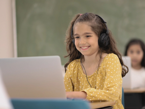 A student listening to a podcast on a laptop in the classroom.