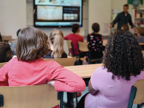 Students in a classroom learning on a SMART board.